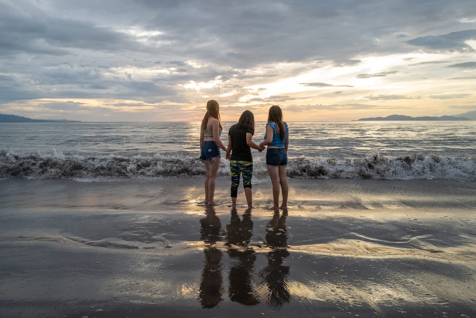 Tres personas tomadas de la mano frente al mar al atardecer